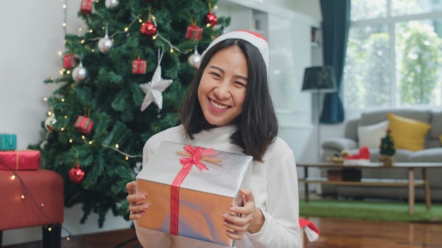 Mulheres asiáticas comemoram o festival de natal. a camisola do desgaste adolescente fêmea e o chapéu do natal relaxam o presente feliz da posse que sorri perto da árvore de natal apreciam as férias de inverno do xmas junto na sala de visitas em casa. Foto gratuita