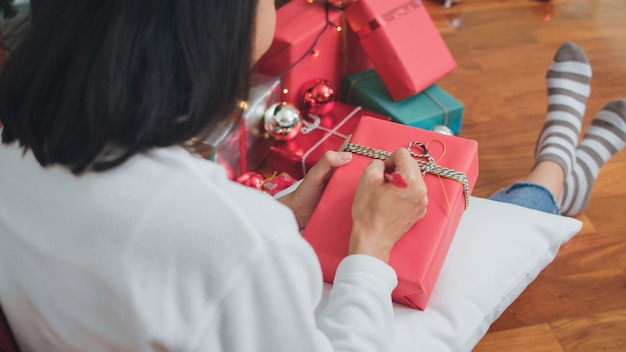 Mulheres asiáticas comemoram o festival de natal. camisola de desgaste adolescente feminino e chapéu de papai noel relaxar feliz escrever um desejo no presente perto de árvore de natal desfrutar de férias de inverno xmas juntos na sala de estar em casa. Foto gratuita