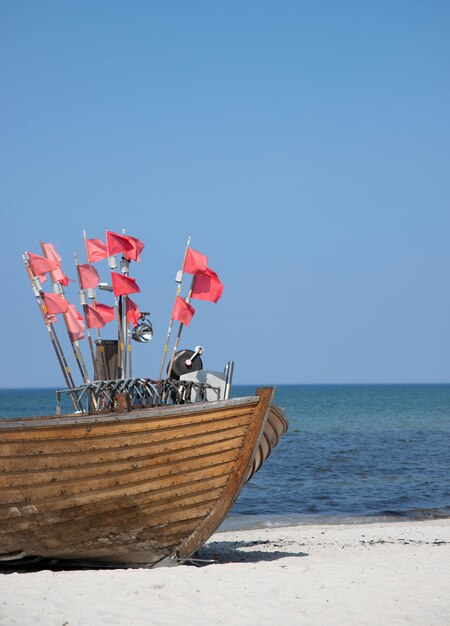 Nariz de barco de pesca em uma praia de areia com várias pequenas bandeiras vermelhas em mastros Foto Premium