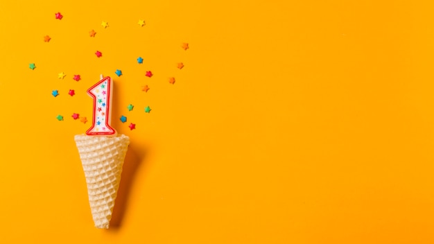 Número 1 vela com estrela colorida granulado sobre o cone de waffle em um pano de fundo laranja Foto gratuita