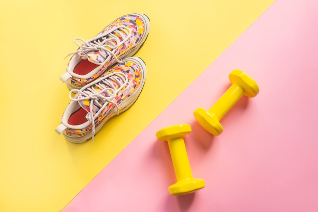 O atleta é ajustado com as sapatilhas running fêmeas e os dumbbells fundo amarelo-cor-de-rosa. Foto Premium