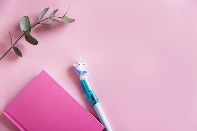 O caderno cor-de-rosa para notas, pena engraçada do unicórnio e eucalipto verde sae no fundo pastel cor-de-rosa. lay plana. vista do topo. espaço da cópia Foto Premium