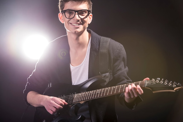 O homem está tocando violão no quarto escuro com luzes atrás dele. Foto Premium