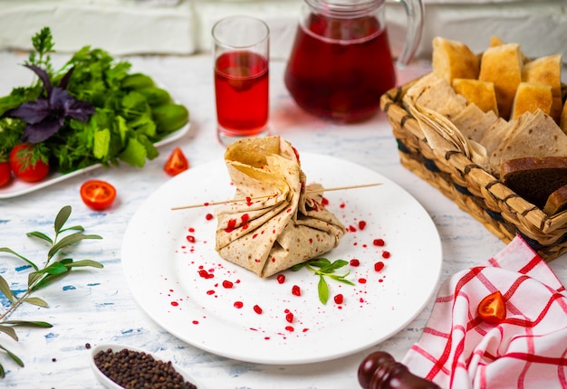 O lanche de lavash rola com as sementes do queijo e do grenate, o pão, os vegetais e o sorvete em uma placa branca. snack Foto gratuita