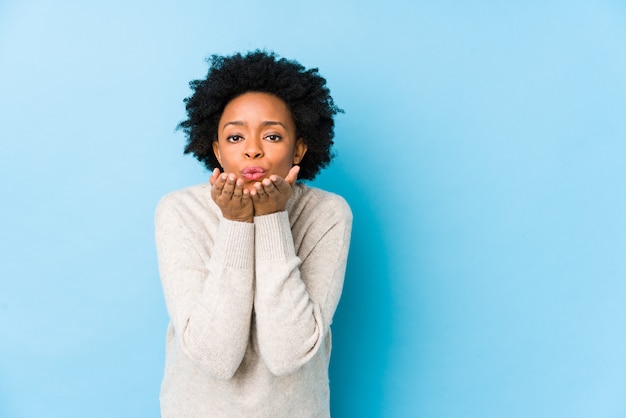 O meio envelheceu a mulher afro-americano contra uma parede azul isolou os bordos de dobramento e guardar as palmas para enviar o beijo do ar. Foto Premium