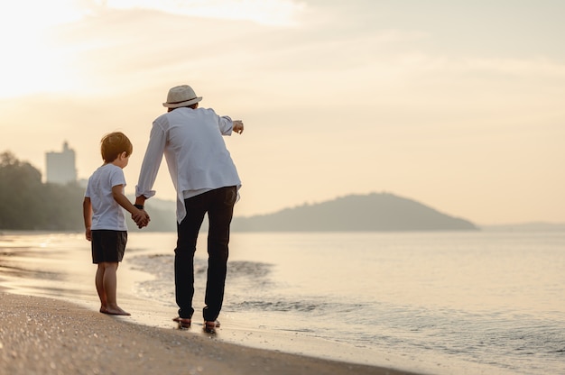 O Pai Está De Mãos Dadas Com Seu Filho E Caminhando Na Praia Ao Pôr Do Sol Em Férias Em Família 2101