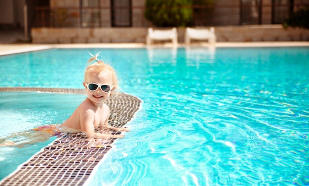 O retrato de um bebê bonito louro nos óculos de sol, nadando na associação em férias de verão. Foto Premium