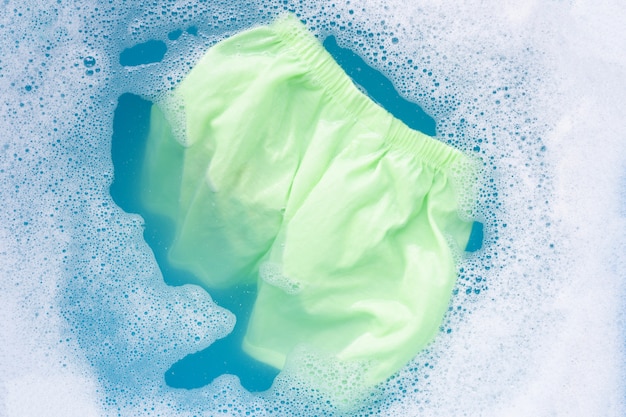 O short verde do bebê embebe na dissolução da água do detergente para a roupa do bebê, pano de lavagem, conceito da lavanderia. Foto Premium