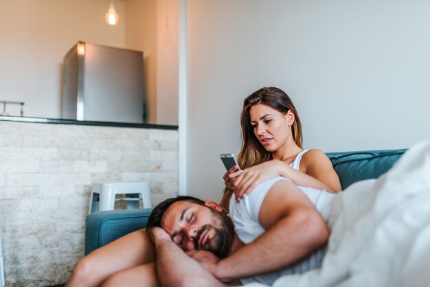 O telefone do namorado cheking da jovem mulher de jelous quando dormir. Foto Premium