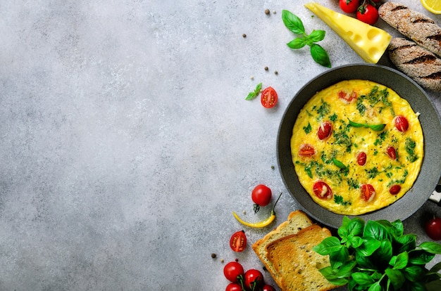 Omelete clássico caseiro com tomate cereja, queijo e ervas no concreto cinzento. frittata em uma frigideira. Foto Premium
