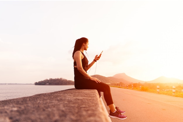 Opinião lateral a mulher do esporte com os fones de ouvido que sentam-se na parede após a corrida da tarde. Foto Premium