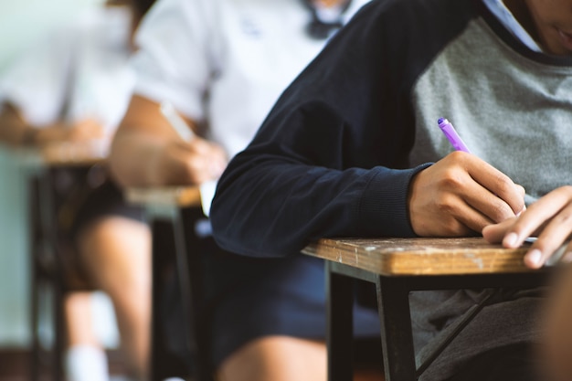 Os estudantes que escrevem a pena à disposição que faz exames respondem às folhas exercitam na sala de aula com esforço. Foto Premium