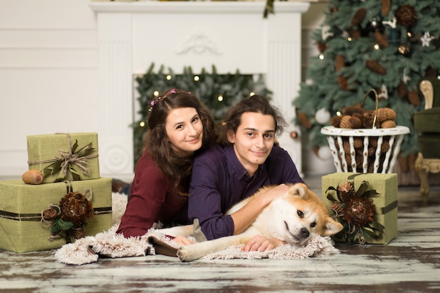 Os pares felizes novos que afagam o cão adorável de akita inu com no assoalho por férias do natal em casa. Foto Premium