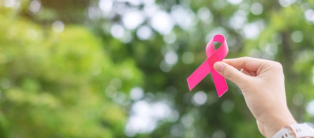 Outubro mês de conscientização do câncer de mama, adulto mão de mulher segurando uma fita rosa com fundo verde para apoiar as pessoas que vivem e doenças. Foto Premium