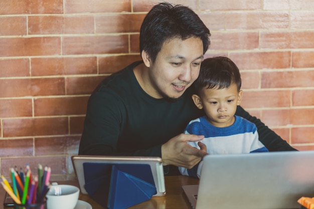 Pai solteira asiática com filho está olhando os desenhos animados via laptop de tecnologia juntos Foto Premium