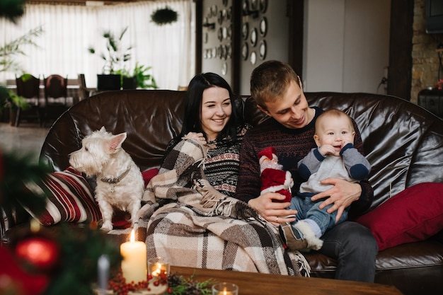 Pais com um bebê no natal e um cão sentado no sofá Foto gratuita
