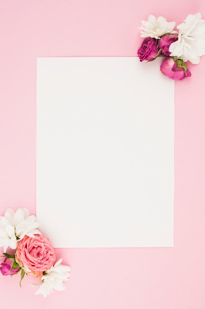 Papel branco em branco com flores frescas contra fundo rosa | Foto Grátis