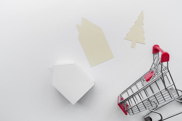 Papel cortado em casa e árvore de natal com modelo de casa em miniatura e carrinho de compras, isolado no fundo branco Foto gratuita