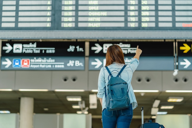 Parte de trás do viajante mulher asiática com pé de bagagem sobre a placa de vôo para check-in Foto Premium