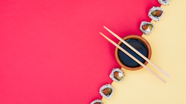 Pauzinhos sobre a tigela de molho de soja com sushi no pano de fundo duplo amarelo e vermelho Foto gratuita