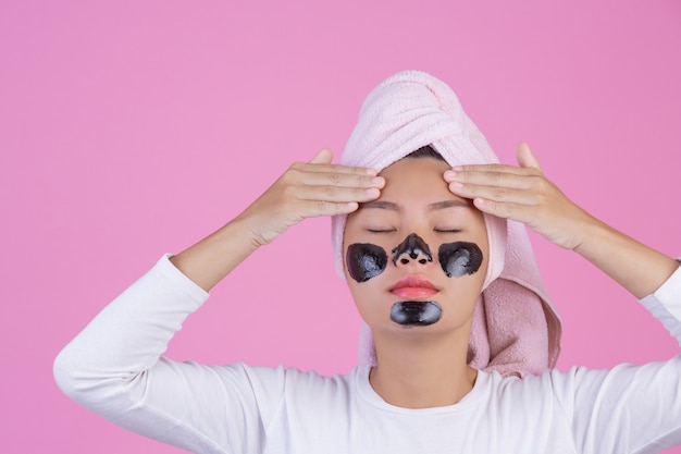 Peeling cosmético de beleza. a fêmea nova com preto retira a máscara no produto cosmético da casca dos cuidados com a pele da pele no rosto em um rosa. Foto gratuita