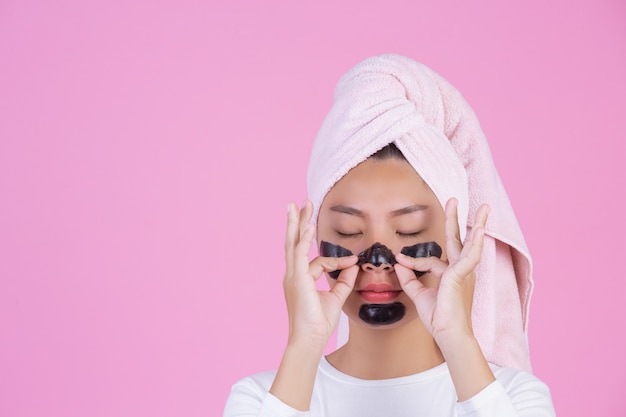 Peeling cosmético de beleza. a fêmea nova com preto retira a máscara no produto cosmético da casca dos cuidados com a pele da pele no rosto em um rosa. Foto gratuita