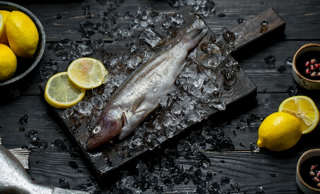 Peixe fresco em uma placa de madeira com cubos de gelo e limão Foto gratuita