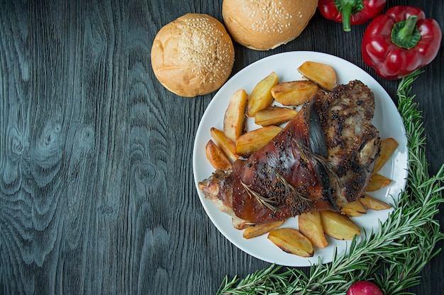 Pernil de porco frito com batatas servido em um prato branco de madeira escura. vista de cima. Foto Premium