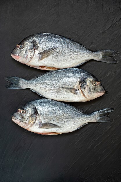 Pescada de peixe cru. filé de peixe cru cinco com tomates frescos orgânicos no gelo no escuro Foto Premium