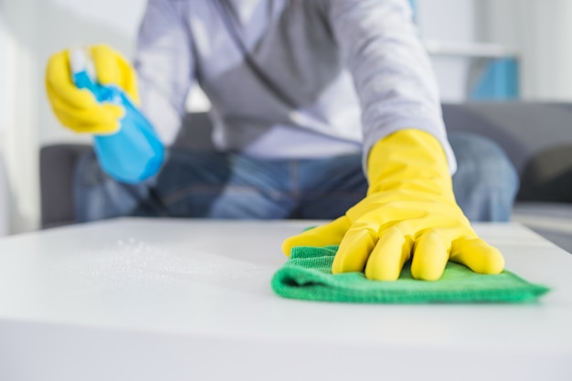 Pessoas, tarefas domésticas e conceito de arrumação - close up of man hands cleaning table with cloth and detergent spray in home Foto gratuita