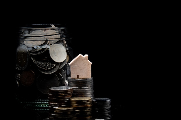 Pilha de moedas e limpar jarra com moeda com casa de madeira no fundo preto Foto Premium