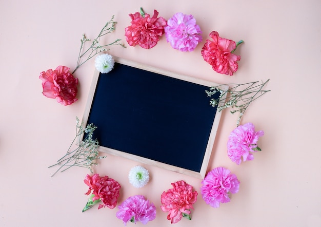 Placa de giz preto com flor cravo fresca no fundo creme suave com espaço de cópia Foto Premium