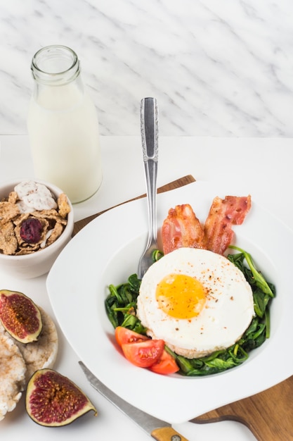 Prato com ovo frito com espinafre; bacon e tomate no fundo branco Foto gratuita
