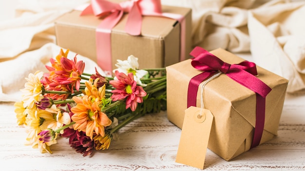 Presente embrulhado marrom com tag vazia e lindo buquê de flores Foto gratuita