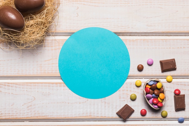Quadro circular azul com chocolates e ovos de páscoa no ninho sobre a mesa de madeira Foto gratuita