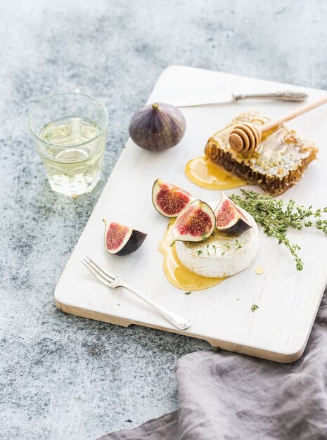 Queijo camembert ou brie com figos frescos, favo de mel e copo de vinho branco na mesa de servir sobre cinza rústico grunge Foto Premium