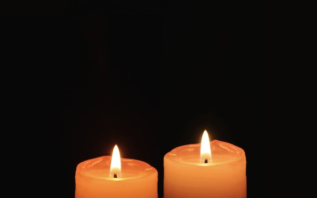 Queimando par de velas laranja em fundo preto Foto Premium