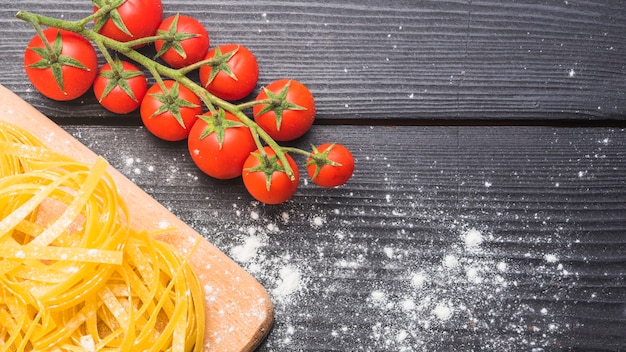 Ramo de tomates cereja maduros com tagliatelle cru polvilhado com farinha no pano de fundo de madeira Foto gratuita
