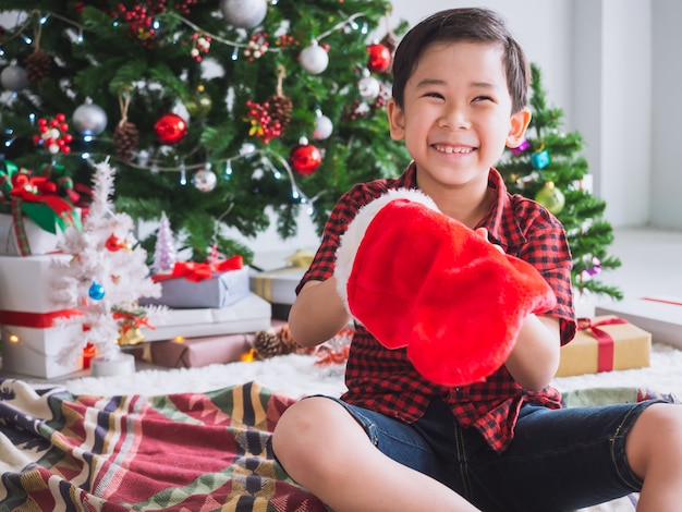 Rapaz de camisa vermelha está segurando a meia vermelha e feliz com engraçado para celebrar o natal com árvore de natal Foto Premium