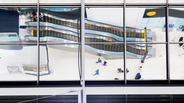 Reflexo de vidro de pessoas de vista superior a pé e sentar escada rolante de escada no aeroporto Foto Premium