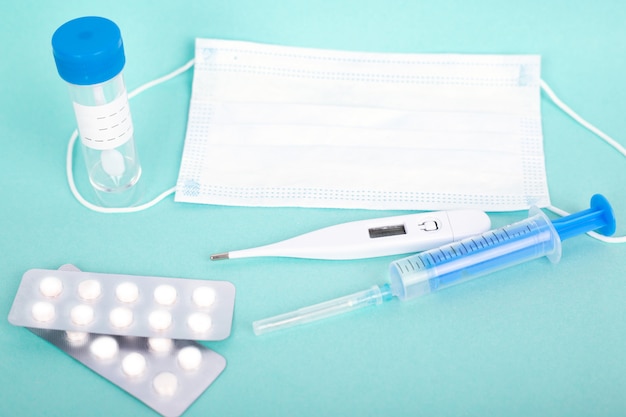 Remédios para resfriado. tubo de ensaio, seringa, pílulas e respirador máscara médica, termômetro sobre fundo azul. | Foto Premium