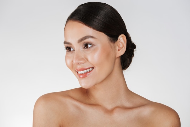 Retrato da beleza da senhora elegante feliz com cabelos castanhos no coque, sorrindo e olhando de lado, isolado sobre o branco Foto gratuita