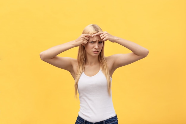 Retrato de close-up da menina preocupada com problema de acne, tocando o rosto, spa, terapia, tratamento, isolado sobre o fundo amarelo Foto Premium