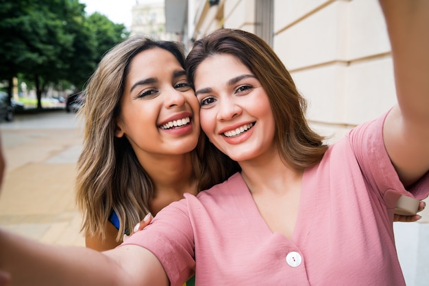 Retrato de dois jovens amigos tirando uma selfie em pé ao ar livre na