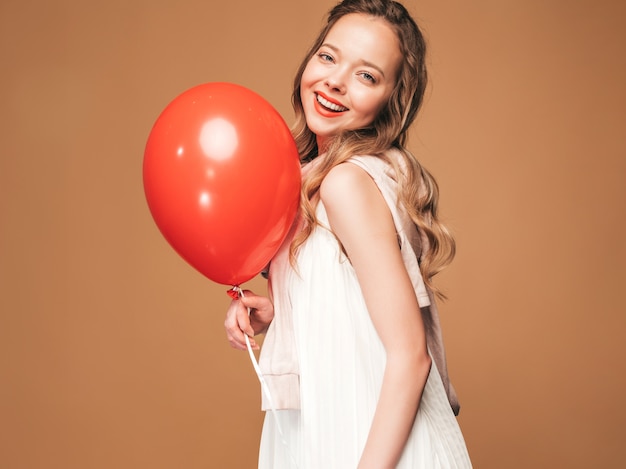 Retrato de jovem animado posando no vestido branco na moda verão. mulher sorridente com balão vermelho posando. modelo pronto para a festa Foto gratuita
