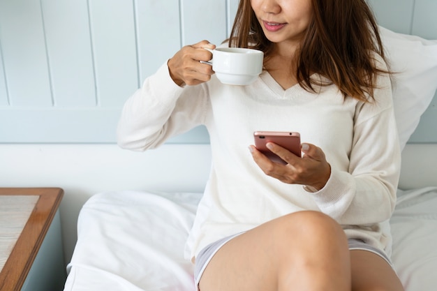 Retrato de mulher usando telefone celular e tomando café enquanto está  sentado na cama de manhã, close-up | Foto Premium