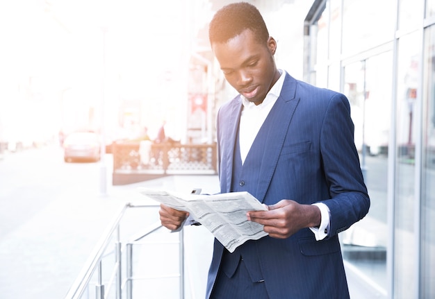 Retrato, de, um, africano, jovem, homem negócios fica, exterior, a, escritório, lendo jornal Foto gratuita
