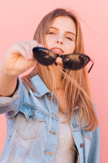 Retrato, de, um, loiro, mulher jovem, segurando, óculos de sol pretos, em, mão, olhando câmera Foto gratuita