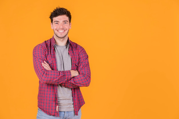 Retrato, de, um, sorrindo, homem jovem, com, seu, braços cruzaram, olhando câmera Foto gratuita