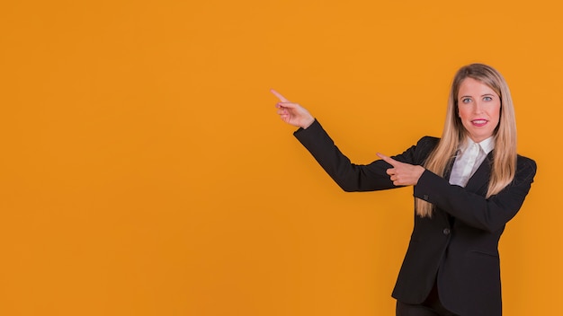 Retrato, de, um, sorrindo, jovem, executiva, apresentando, algo, contra, um, fundo laranja Foto gratuita